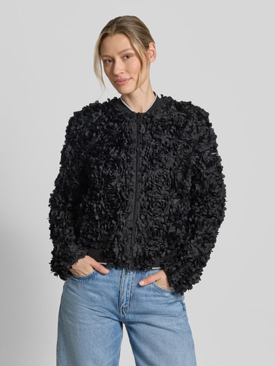 Frauenmodel trägt Blouson mit Label-Patch Modell 'JADE' von Frieda & Freddies in Schwarz, Gerader-Schnitt, Stehkragen, Zweiwege-Reißverschluss, gerippter Saumabschluss, strukturierte 3D-Rosen-Textur, Rückenlänge 53 cm, Schulterbreite 40 cm, Brustweite 50 cm, Ärmellänge 65 cm, Ganzkörperansicht von vorne.