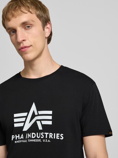 Männermodel trägt schwarzes T-Shirt mit Logo und Rundhalsausschnitt von Alpha Industries aus reiner Baumwolle, Nahaufnahme Oberkörper.