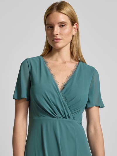 Frauenmodel trägt Damen Abendkleid mit Spitzenbesatz von Christian Berg Cocktail in Türkis, V-Ausschnitt, Wickel-Optik, Nahaufnahme Oberkörper.