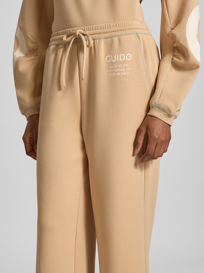 Frauenmodel trägt Wide Fit Sweatpants aus Baumwoll-Mix Modell 'Gunda' von GUIDO MARIA KRETSCHMER WOMAN in Beige mit Logo-Print, elastischem Bund und Eingrifftaschen, Nahaufnahme Oberkörper.