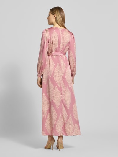 Frauenmodel trägt Regular Fit sukienka wieczorowa z satyny model 'Bretti' z wzorem paisley na całej powierzchni od Neo Noir, taliowany fason z odpinaną materiałową tasiemką, długie rękawy, całkowita długość tyłu w rozmiarze 36: 131 cm, szerokość w rozmiarze 36: 48 cm, długość rękawów w rozmiarze 36: 63 cm, kopertowy styl, jasnoróżowe i kremowe kolory, satynowa powierzchnia, widok całej sylwetki z tyłu.
