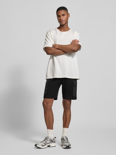 Męski model nosi Regular Fit Shorts mit Cargo-Taschen von Antony Morato, mieszanka bawełny, wpuszczane i tylne kieszenie, czarne, krój regular fit, długość wewnętrzna nogawki 23 cm w rozmiarze M, widok całej sylwetki z przodu.
