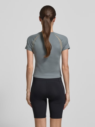 Frauenmodel trägt T-Shirt mit Mesh-Einsätzen und Logo von Under Armour, Material-Mix mit Stretch-Anteil, Cropped, Rückenlänge 45 cm, Ganzkörperansicht Rückansicht.