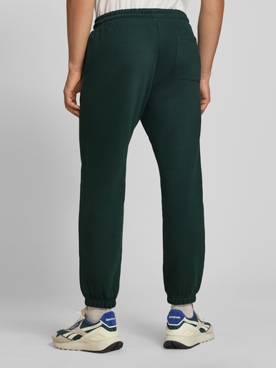 Männermodel trägt Straight Fit Sweatpants aus Baumwoll-Mix Modell 'Kane' von JACK & JONES in Dunkelgrün, elastischer Bund und Beinabschlüsse, Gesäßtasche, Logo-Detail, Ganzkörperansicht Rückansicht.