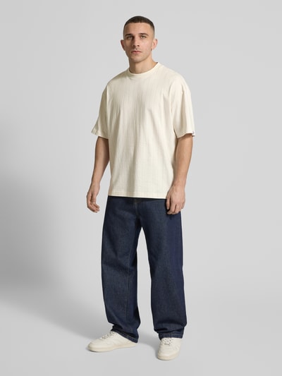 Männermodel trägt Regular Fit T-Shirt aus reiner Baumwolle Modell 'NORAYATI' von Hugo Blue mit Allover-Muster, gestreift, Jersey, Rundhals, Kurzarm, Label Smiley Print, in Creme und Blau, Ganzkörperansicht von vorne.