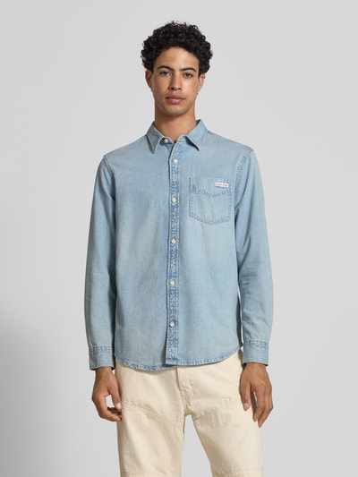 Männermodel trägt Regular Fit Jeanshemd aus reine Baumwolle von Calvin Klein Jeans in denimlook met labelpatch op borstzak, lichte blauwe kleur, lange mouwen met manchet met één knoop, kentkraag, doorlopende knoopsluiting, materiaal puur katoen, ganzkörperansicht von vorne.