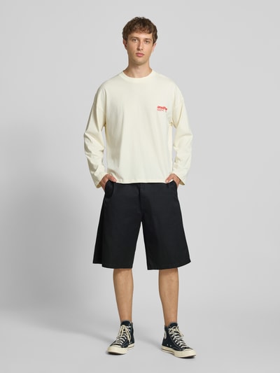 Männermodel trägt schwarze Bermudas mit Baumwoll-Anteil Modell 'Brader' von Carhartt Work In Progress, Relaxed Fit, Ganzkörperansicht von vorne. Materialmix, Eingriff- und Gesäßtaschen, Gürtelschlaufen, Knopf- und Reißverschluss.