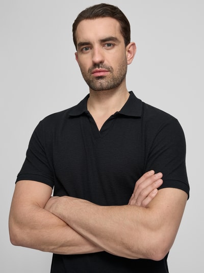 Männermodel trägt Comfort Fit Poloshirt mit V-Ausschnitt von Lindbergh aus Reine Baumwolle, Schwarz, Strukturmuster, Label-Detail, Nahaufnahme Oberkörper.