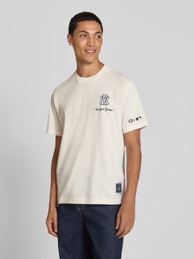 Männermodel trägt Relaxed Fit T-Shirt aus reiner Baumwolle von Champion in Beige mit Statement-Print, Ganzkörperansicht von vorne.