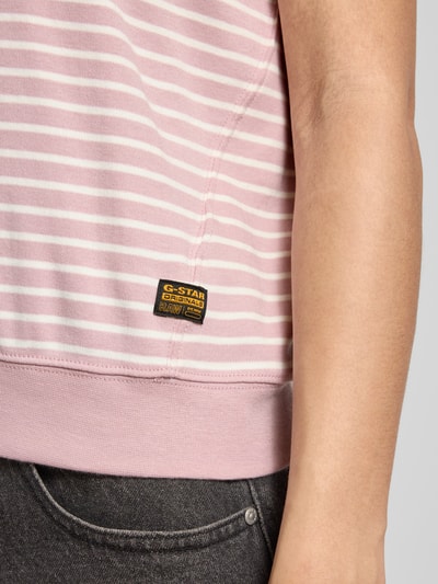 Kobiece modelka nosi Relaxed Fit T-Shirt aus Baumwoll-Mix mit Label-Patch od G-Star Raw, pastelowe różowo-białe paski, bawełna z elastanem, elastyczny dół, krótki rękaw, naszywka z logo, zbliżenie na dolną część torsu.