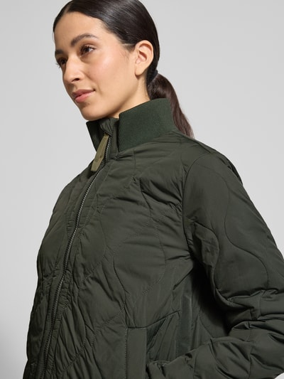 Vrouwenmodel draagt Steppjacke mit Stehkragen van camel active in donkergroen, rechte fit, met elastische mouwboorden, Nahaufnahme bovenlichaam.