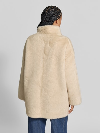 Vrouwenmodel draagt Kunstfelljacke mit Stehkragen van Juvia, imitatiebont in lichtbeige, lichte a-lijn, afdekstrip, ruglengte maat S 80 cm, borstwijdte maat S 50 cm, mouwlengte maat S 62 cm. Volledig aanzicht achteraan.