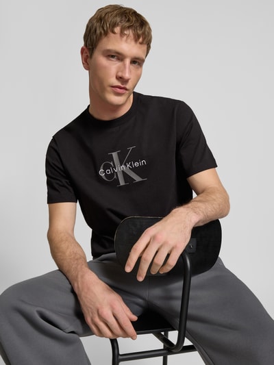 Männermodel trägt T-Shirt mit Label-Print und Rundhalsausschnitt von Calvin Klein Jeans in Schwarz, Reine Baumwolle, Regular-Fit, Nahaufnahme Oberkörper.