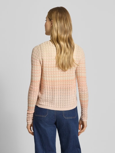 Frauenmodel trägt Strickjacke aus Viskose-Mix Modell 'ROSALYN' von Guess, Gerader-Schnitt, V-Ausschnitt, Knopfverschluss, Rückenlänge 51 cm, Ärmellänge 69 cm, dezente Rosa- und Beigetöne, feine Strickstruktur, Ganzkörperansicht Rückansicht.