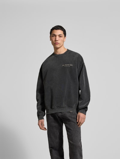 Männermodel trägt Oversized Sweatshirt aus Baumwoll-Mix von Don't Waste Culture in Dunkelgrau mit Statement-Print, elastische Abschlüsse, Ganzkörperansicht von vorne. Rückenlänge bei Größe M: 67 cm.