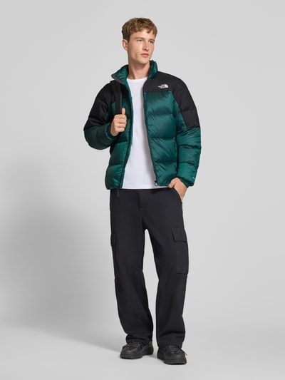 Männermodel trägt Regular Fit Jacke mit Daunen-Feder-Füllung Modell 'Diabolo' von The North Face, Stepp-Optik, Stehkragen, Logo-Stitching, grün und schwarz, ganzkörperansicht von vorne.