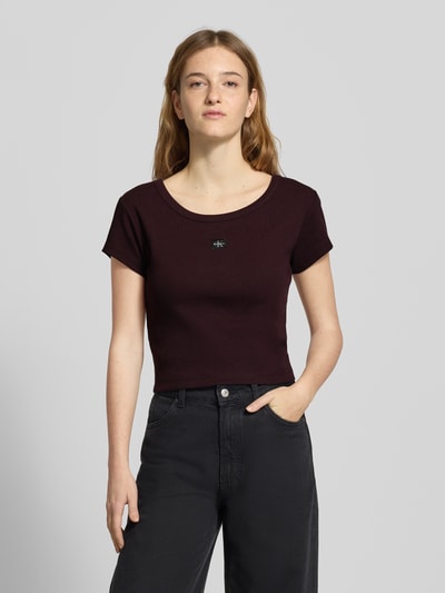 Modelka kobieca ma na sobie Cropped T-Shirt mit Label-Detail od Calvin Klein Jeans, kolor bordowy, bawełna z domieszką elastanu, widok całej sylwetki z przodu.