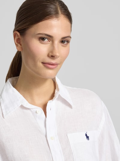 Frauenmodel trägt Oversized Hemdbluse aus reinem Leinen von Polo Ralph Lauren in Weiß, feine Textur, sichtbares Logo-Stitching, Nahaufnahme Oberkörper.