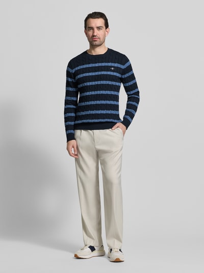 Männermodel trägt Slim Fit Pullover in Strick-Optik von Gant in Dunkelblau mit hellblauen Streifen, Baumwolle, Logo-Stitching, Ganzkörperansicht von vorne.