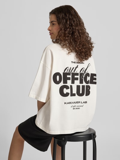 Kobiece model prezentuje Cropped Oversized T-Shirt mit Label-Print von Karo Kauer, damski t-shirt z bawełny, krój oversized, krój krótki, nadruk z logo z przodu i z tyłu, okrągły dekolt, długość tyłu w rozmiarze S: 60 cm, Ganzkörperansicht Rückansicht.