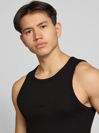 Męski model nosi Tanktop mit Logo-Stitching Modell 'The Embroidery' von PROHIBITED, czarny, delikatny prążkowany wzór, okrągły dekolt, przylegający krój, bawełniany materiał ze stretch-em; kontekst: Herren Tanktop von PROHIBITED, Körpernaher Schnitt, Feinripp, Rundhalsausschnitt, Logo-Stitching, długość tyłu w rozmiarze M: 56 cm; zbliżenie na górną część ciała