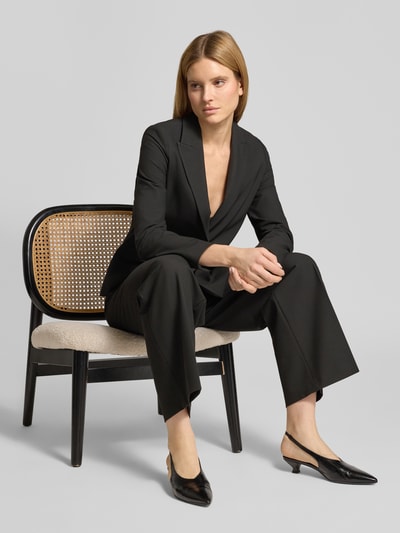Vrouwenmodel draagt Wide Leg stoffen broek met persplooien van s.Oliver BLACK LABEL, look: effen, pasvorm: wide leg, met riemlussen, schiehaak- en verborgen ritssluiting, elastische boord, zij-instapzakken en aangezette achterzakken, geheel zwart, detailopname van vooraan.