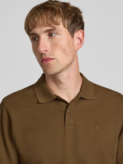 Męski model nosi Slim Fit Poloshirt mit Label-Stitching Modell 'AUSTIN' von JACK & JONES, mieszanka materiałów z bawełną, kołnierzyk polo, wyhaftowane logo, długość tyłu w rozmiarze M: 70 cm, zbliżenie na górną część ciała.