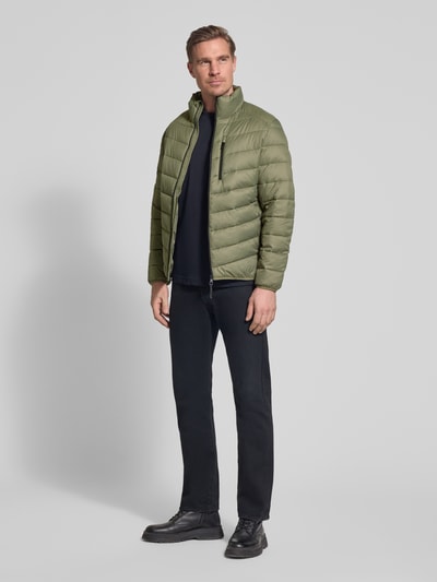 Męski model nosi Regular Fit Steppjacke mit vertikaler Reißverschlussbrusttasche von Tom Tailor Denim, efekt: jednolity kolor, krój regular fit, stójka, zapięcie na zamek błyskawiczny, długi rękaw, zakończenia z wypustkami, pionowa kieszeń na zamek, wpuszczane kieszenie, zielona, faktura pikowana; całopostaciowy widok z przodu.