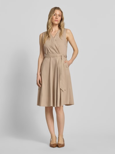 Frauenmodel trägt Kleid mit V-Ausschnitt in Wickel-Optik von More & More, Beige, Baumwoll-Mix, Tailliert, Ärmelloses-Design, Taillenband, Ganzkörperansicht von vorne.
