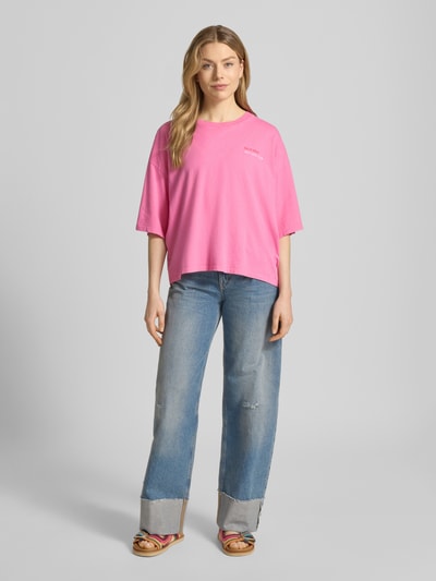 Frauenmodel trägt T-Shirt mit rückseitigem Motiv-Print Modell 'NICA' von ICHI in Pink, lockerer Schnitt, Jeans, Ganzkörperansicht von vorne, reine Baumwolle, Rundhalsausschnitt, Statement-Print und -Stitching, überschnittene Schultern.