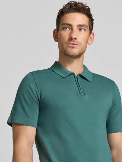 Männermodel trägt Regular Fit Poloshirt mit Reißverschluss Modell 'MILANO' von Jack & Jones Premium in grün, Nahaufnahme Oberkörper. Bio-Baumwoll-Mix, Polokragen, Label-Detail.