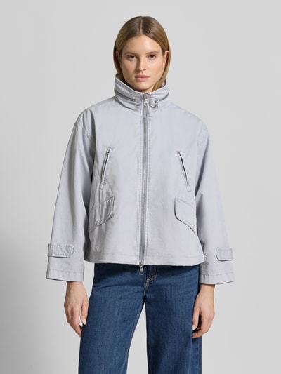 Kobiece model nosi kurtkę z bawełny o luźnym kroju ze stójką, zamek błyskawiczny dwustronny, wpuszczane kieszenie. Jacke mit Stehkragen od Blonde No. 8, długość tyłu w rozmiarze 36: 61 cm, szerokość ramion: 51 cm, szerokość klatki piersiowej: 60 cm, długość rękawów: 60 cm. Ganzkörperansicht von vorne.