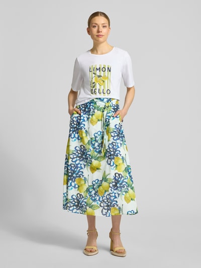 Frauenmodel trägt Regular Fit Midirock mit floralem Allover-Print von More & More, reine Baumwolle, A-Linie, Weiß mit buntem Muster, Ganzkörperansicht von vorne.