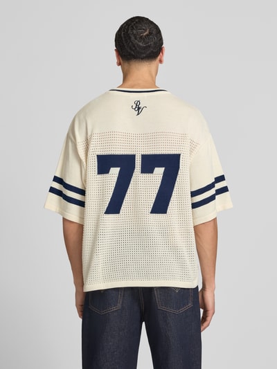 Męski model nosi Strick-Trikot mit Jacquard Muster von REVIEW, prosty krój, dekolt w serek, rękaw o dł. 1/2, perforowanie, długość tyłu w rozmiarze M: 69 cm, kremowy z granatowymi detalami, ażurowy wzór, całkowity widok z tyłu.