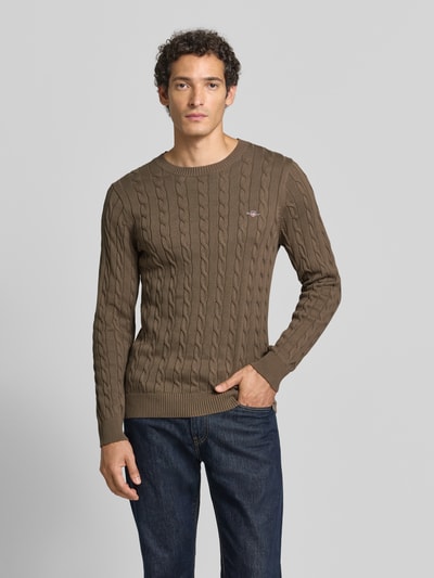 Männermodel trägt Regular Fit Pullover aus reiner Baumwolle von GANT in Braun mit Zopfstrickmuster, Herren Pullover, Ganzkörperansicht von vorne.