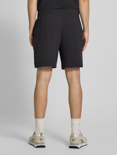 Männermodel trägt Shorts mit Logo-Stitching von PUMA PERFORMANCE in Schwarz mit Strukturmuster aus Reine Baumwolle, Gerader-Schnitt, Elastischer-Bund, Ganzkörperansicht Rückansicht.