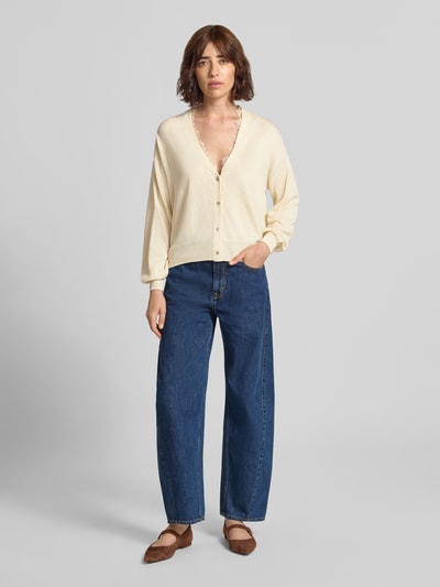 Modelka nosi kardigan z dekoltem w serek i obszyciem koronką od Jake*s Casual, mieszanka materiałów z lnem, krój regular fit, listwa guzikowa, długość tyłu w rozmiarze S: 55 cm, długość rękawów: 49 cm, kremowy, gładka faktura; całkowity widok z przodu.