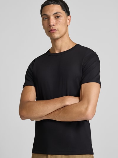 Męski model nosi Regular Fit T-Shirt aus Baumwoll-Mix von JACK & JONES, elastyczna mieszanka bawełny, okrągły dekolt, krótki rękaw, długość tyłu w rozmiarze M 67 cm, jednolity czarny kolor, gładka tekstura, krój regular fit, zdjęcie całej sylwetki z przodu.