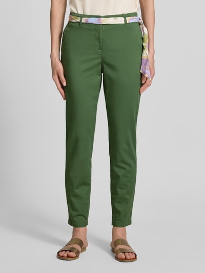 Kobiece model nosi Slim Fit Chino mit Viskose-Anteil od Christian Berg Woman, zielone, mieszanka bawełny i wiskozy, krój slim fit, skrócony, odpinana materiałowa tasiemka, zapięcie na guzik i zamek błyskawiczny, widok na całe ciało z przodu.