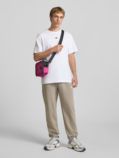 Männermodel trägt Sweatpants mit Logo-Print von The North Face aus Baumwoll-Mix, Slim-Fit, elastischer Bund mit Kordelzug, elastische Abschlüsse, hellbeige Farbe, glatte Textur, Innenbeinlänge bei Größe M 70 cm, Ganzkörperansicht von vorne.