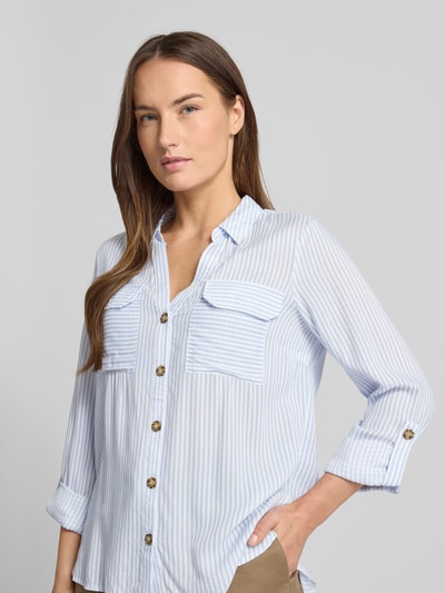 Vrouwenmodel draagt Relaxed Fit Hemdbluse aus reiner Viskose Modell 'BUMPY' van Vero Moda, gestreept blauw-wit, borstzakken, hemdkraag, Two Tone, lange mouwen met turn-up, knoopsluiting, ganzkörperansicht van voren.