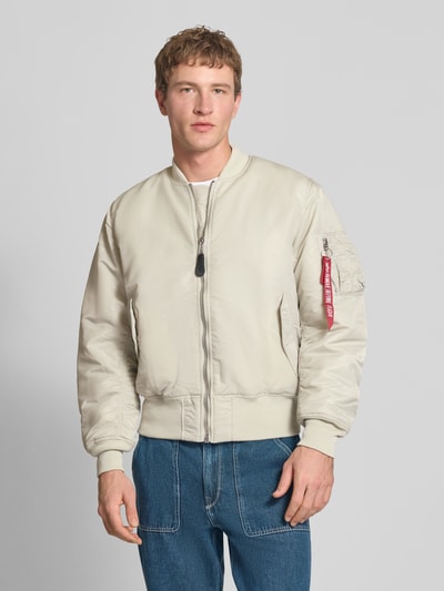Männermodel trägt Regular Fit Bomberjacke mit Stehkragen Modell 'Heritage' von Alpha Industries in Beige mit Reißverschluss, Pattentaschen, elastischen Abschlüssen, Rückenlänge 63 cm, Schulterbreite 50 cm, Brustweite 57 cm, Nahaufnahme Oberkörper.