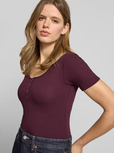 Kobiece model nosi Slim Fit T-Shirt aus Baumwoll-Mix Modell 'KITTE' von Pieces, efekt: jednolity kolor, krój slim fit, dekolt w łódkę, dekolt henley, rękaw: krótki rękaw, wykończenie materiału: prążkowana faktura, materiał: mieszanka bawełny, zbliżenie na górną część ciała z przodu.