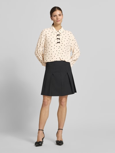 Frauenmodel trägt Regular Fit Hemdbluse aus reiner Viskose Modell 'Lovy' von FREE/QUENT, cremefarben mit schwarzen Punkten und Zierschleifen, Hemdblusenkragen, langärmlig, kombiniert mit schwarzem Rock, Ganzkörperansicht von vorne.