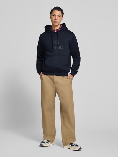 Männermodel trägt Hoodie aus Baumwoll-Mix Modell 'FREDERIKS' von JACK & JONES in Dunkelblau mit Label-Print, lockere Passform, Ganzkörperansicht von vorne.