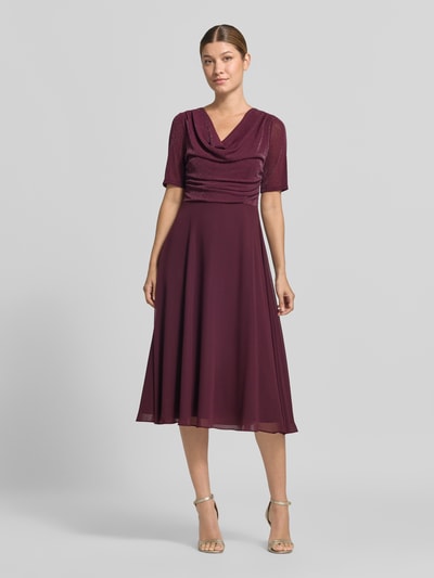 Kobiece model prezentuje Fit and Flare Cocktailkleid mit Wasserfallausschnitt od Vera Mont, sukienka koktajlowa w kolorze bordowym, gładka tekstura, cała sylwetka z przodu.