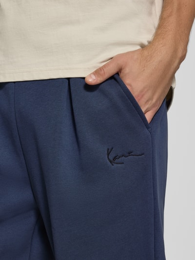 Männermodel trägt Sweatpants mit Logo-Stitching und Eingrifftaschen von Karl Kani in Dunkelblau, Baumwoll-Mix, Nahaufnahme Oberkörper.