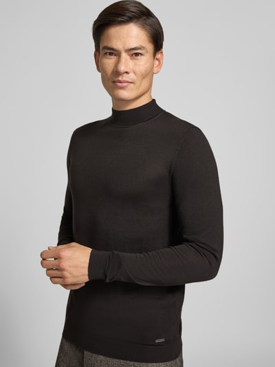 Männermodel trägt schwarzen Strickpullover aus Schurwolle mit Stehkragen von ROY ROBSON, Slim Fit, Label-Detail, Ganzkörperansicht von vorne.