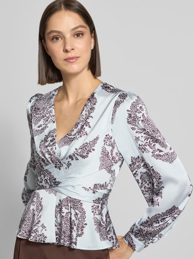 Vrouwenmodel draagt blouse met Peplum-zoom model 'Rista' van Neo Noir, getailleerde pasvorm, v-hals, met lange mouwen, ruglengte maat 36: 55 cm, mouwlengte maat 36: 65 cm, lichtblauw met donker bordeaux patroon, detailopname bovenlichaam.