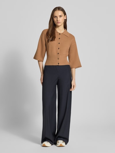 Frauenmodel trägt Strickjacke aus Viskose-Mix Modell 'SHYLA' von Noisy May in lockerer Passform, Umlegekragen, 3/4-Arm, gerippte Abschlüsse, durchgehende Knopfleiste, Rückenlänge 48 cm, einfarbiges Design, Ganzkörperansicht von vorne.